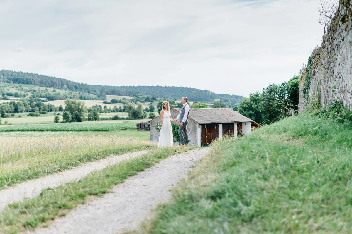 Brautpaar auf einem malerischen Weg vor ländlicher Kulisse.