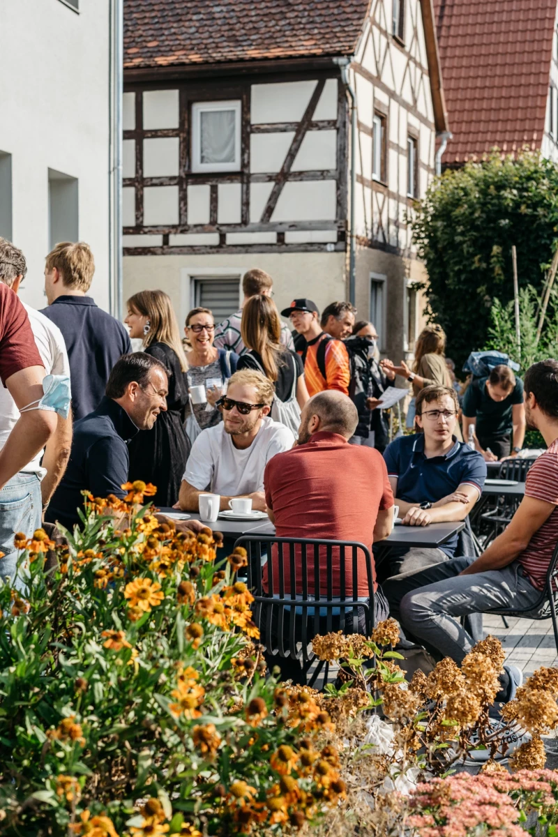 Menschen genießen Kaffee und Gespräche im Freien vor dem Schwarzen Adler.